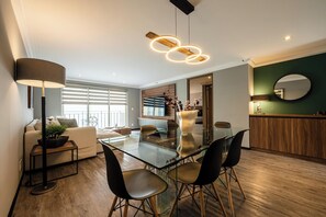 A modern dining area with a glass table, black chairs, and a unique pendant light. - Capitalia Living Apartments J Verne (Mexico City)