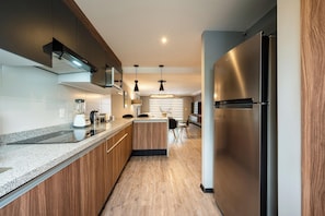A modern kitchen with wooden cabinets, a stainless steel refrigerator, a built-in island, and a dining area with a table and chairs. - Capitalia Living Apartments J Verne (Mexico City)