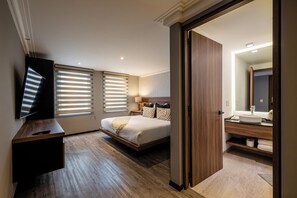 Una habitación de hotel moderna con cama, escritorio, televisor y baño con espejo y lavamanos.