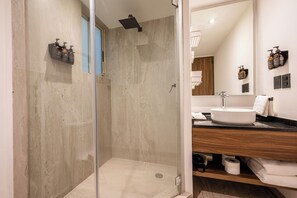 A modern bathroom with a glass-enclosed shower, a white sink, and a wooden vanity. - Capitalia Living Apartments J Verne (Mexico City)
