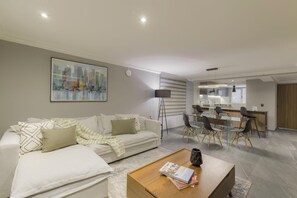 A modern living room with a sofa, coffee table, and a dining area with a glass table and chairs. - Capitalia Living Apartments J Verne (Mexico City)