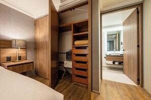 A modern bedroom with a wooden wardrobe, a bedside table with a lamp, and a view into a bathroom with a mirror and sink. - Capitalia Living Apartments J Verne (Mexico City)