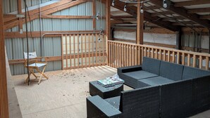 Un espacio en el ático con una terraza de madera, un sofá de mimbre negro y una silla de madera.