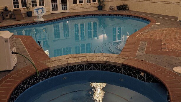 Una piscina interior con borde de azulejos, un jacuzzi y un ventilador de techo.