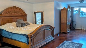 Un dormitorio con cama de madera, ventilador de techo, un espejo grande y vista al exterior por una ventana.