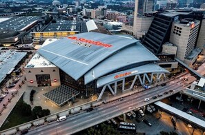 An aerial view of the State Farm Arena with its distinctive curved roof and surrounding urban landscape.