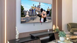 Un televisore fissato alla parete con un'immagine di un personaggio Disney, un tavolino consolle in legno scuro e una poltrona confortevole.