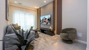 Un soggiorno moderno con una televisione a schermo piatto, un divano, una poltrona, un tavolino da caffè e una pianta grande.