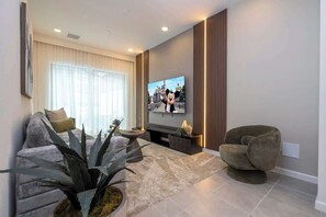 Una sala de estar moderna con un televisor de pantalla plana, un sofá, un sillón, una mesa de centro y una planta grande.