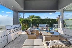 Eine Außenküche mit Grill, Korbmöbeln und Blick auf einen Swimmingpool.