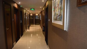 Ein Hotelgang mit Türen auf beiden Seiten, einem Feuerlöscher an der rechten Wand und einem gerahmten Kunstwerk über den Türen.