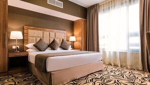 Ein Hotelzimmer mit einem großen Bett, zwei Nachttischen mit Lampen, einem gemusterten Teppich und einem Fenster mit Vorhängen.