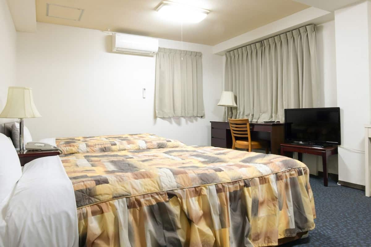 A hotel room with a bed, a desk, a television, and a window with curtains.