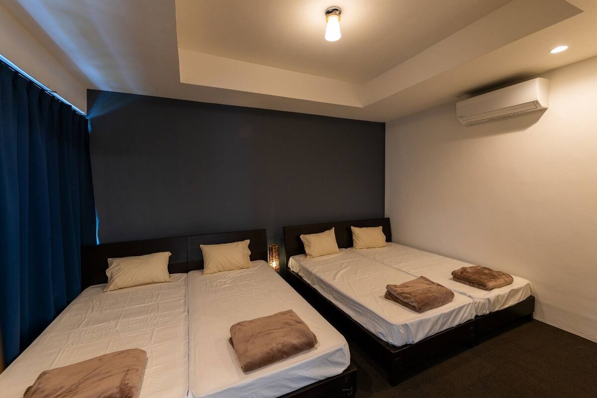 Une chambre d’hôtel avec deux lits, des murs sombres, un climatiseur et un luminaire au plafond.