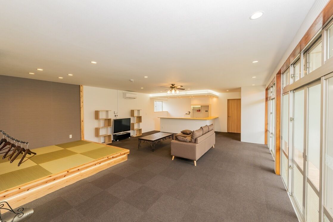 Un vaste espace de vie comprenant un tatami, un canapé, une télévision et un ventilateur de plafond.