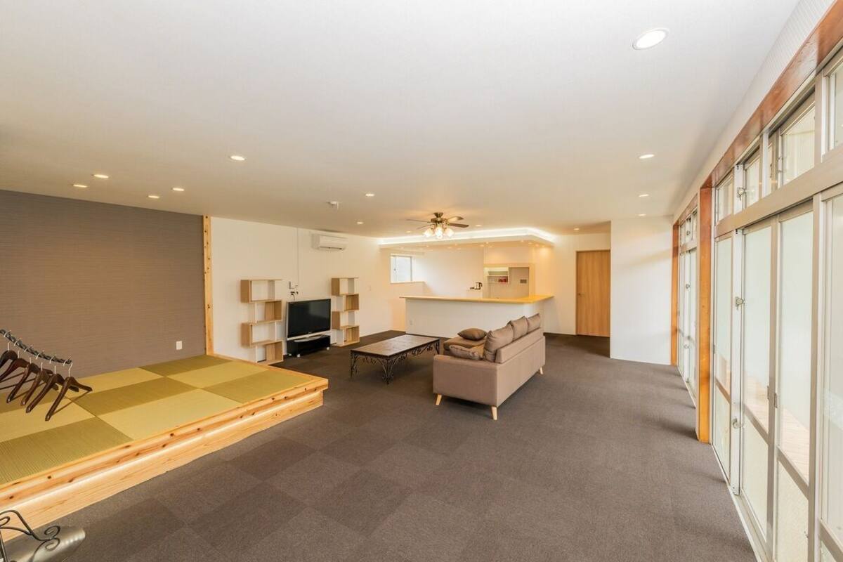 Un vaste espace de vie comprenant un tatami, un canapé, une télévision et un ventilateur de plafond.