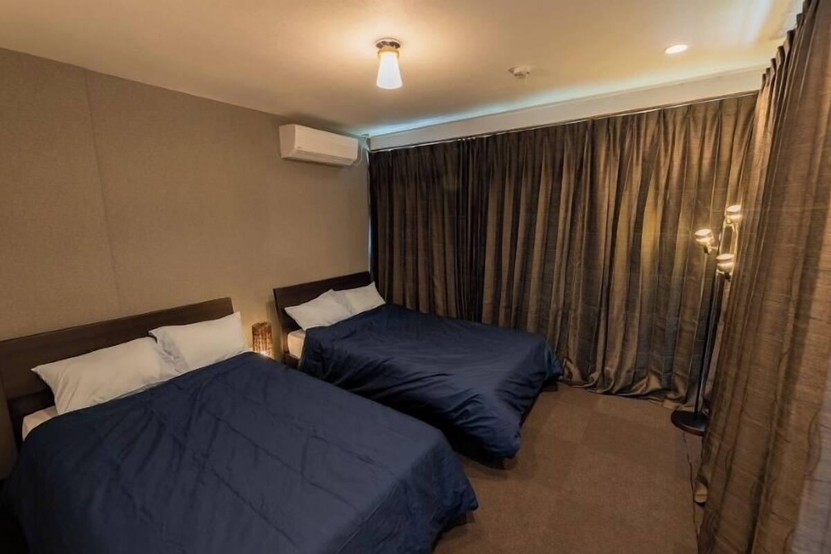 Une chambre d’hôtel avec deux lits, un luminaire au plafond, un appareil de climatisation et un rideau.