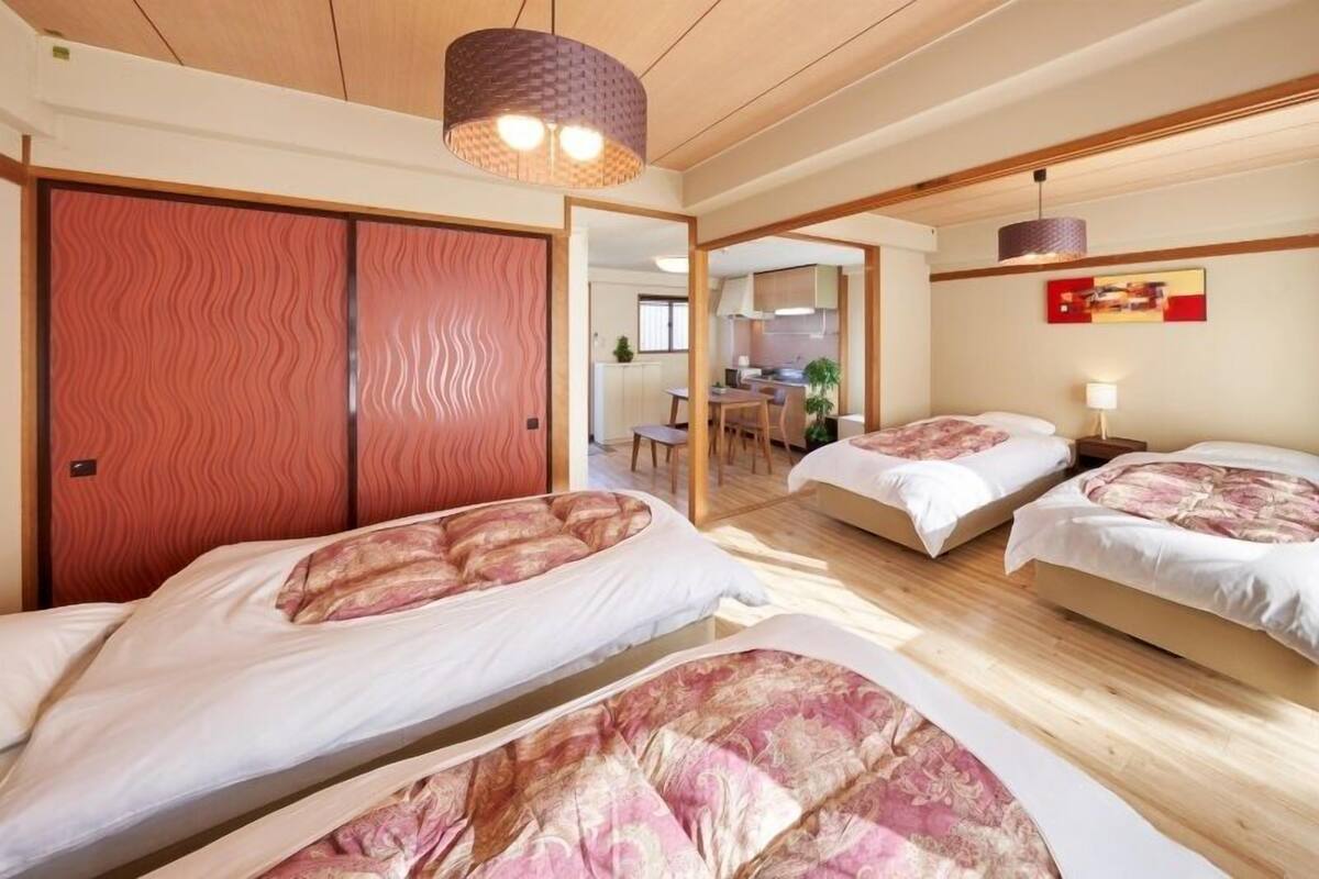 Ein Hotelzimmer mit zwei Betten, einer Holzbalkendecke und einem durch eine geöffnete Tür einsehbaren Küchenbereich.