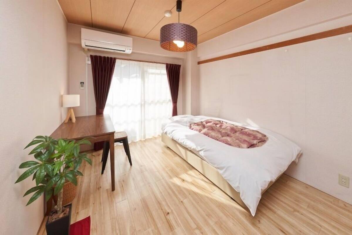 Ein Zimmer mit einem Bett, einem Schreibtisch, einer Zimmerpflanze und einer Klimaanlage.