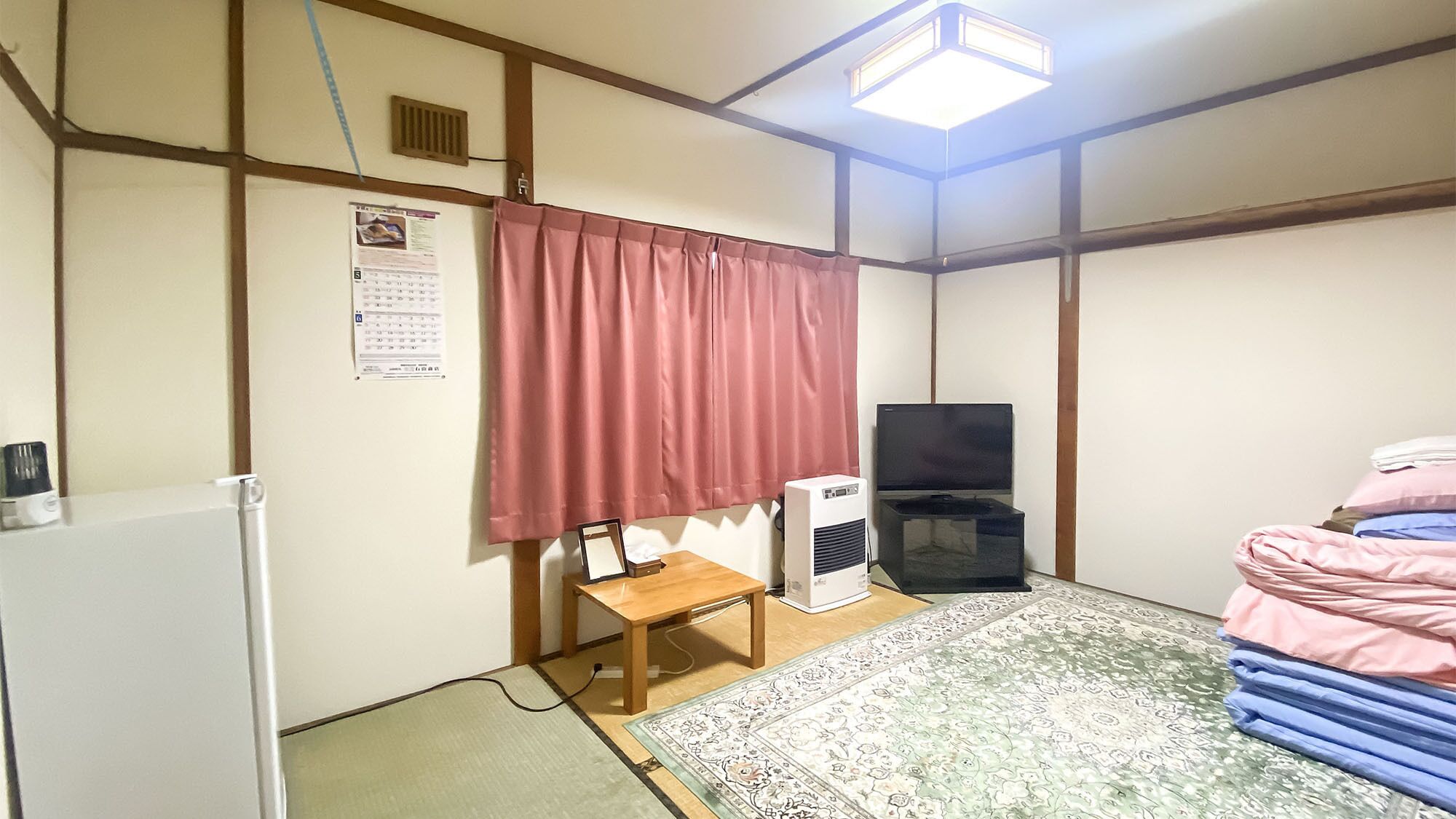 Una habitación con cama, una mesita, un calefactor, un televisor y un calendario en la pared.