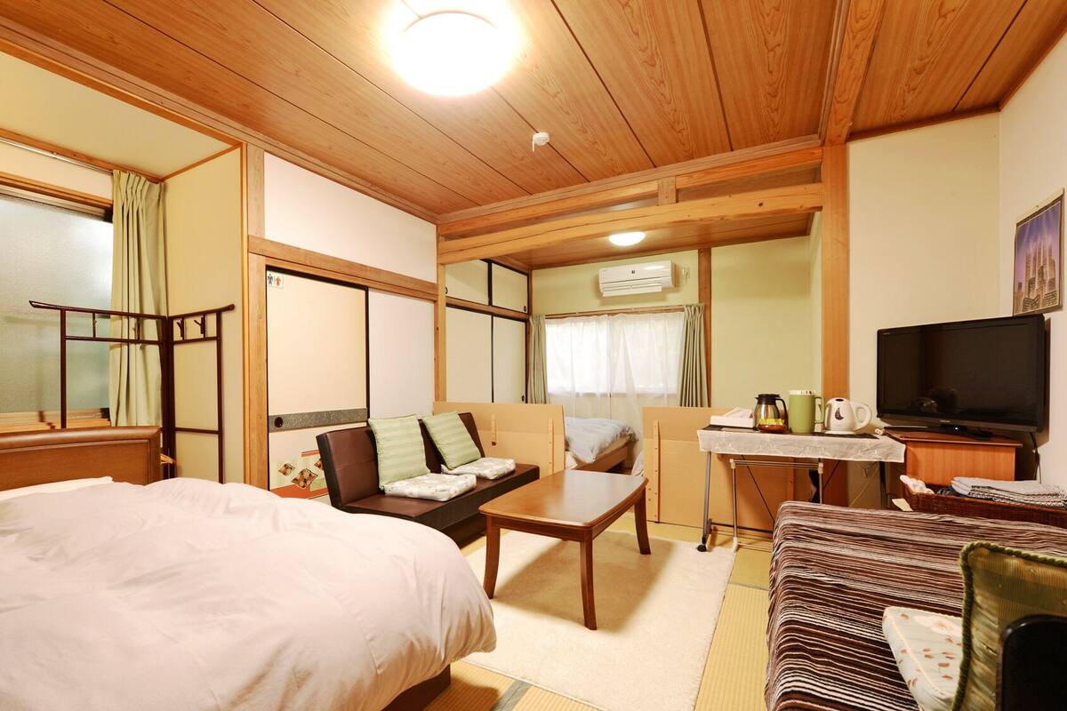 Habitación de hotel pequeña con cama, sofá, una mesita, televisor y aire acondicionado.