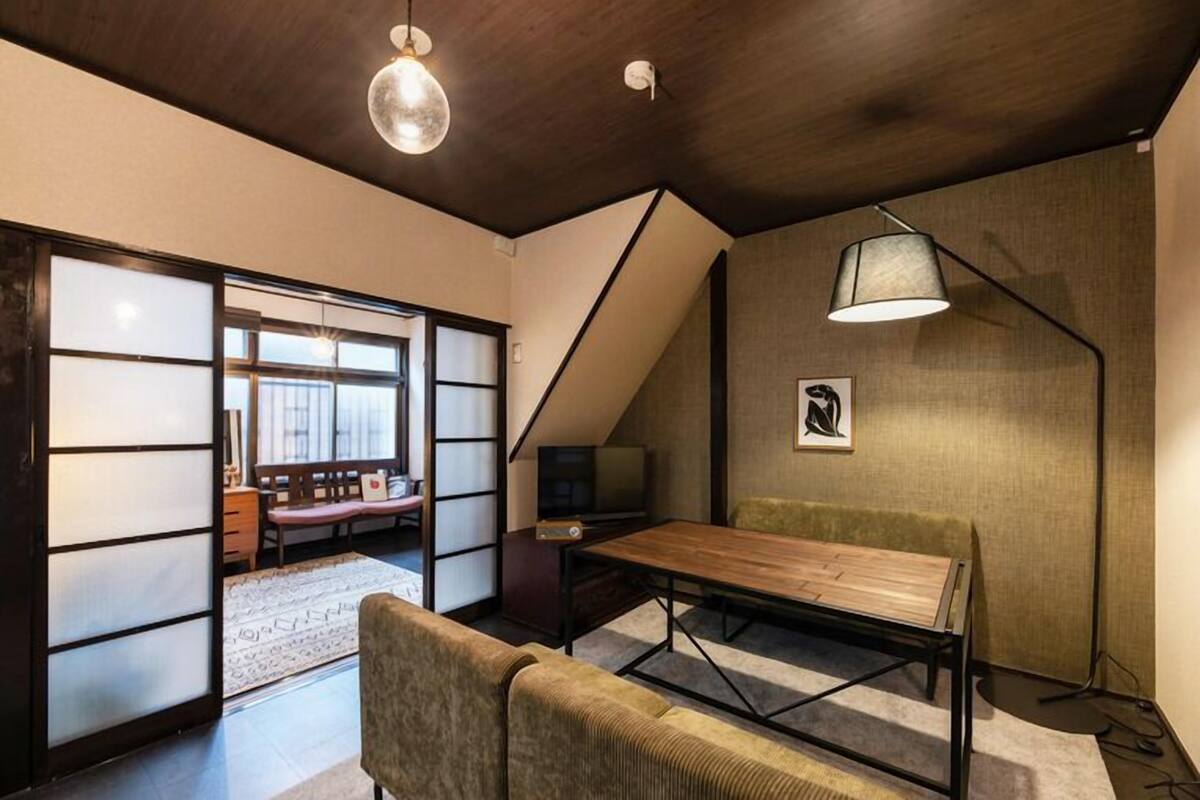 A room with a low ceiling, a wooden table, a sofa, a TV, and a lamp.