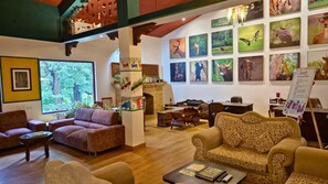 A spacious lounge area with multiple seating options, including sofas and chairs, a fireplace, and a wall adorned with wildlife-themed artwork. - Tathastu Kanha -the Serenity Retreat (Baihar)