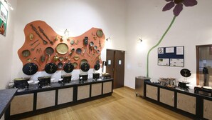 Habitación con una exhibición central de utensilios de cocina y vajilla en una pared curva, un mostrador de buffet con diferentes platos y un cartel de 'No Fumar' en la pared.