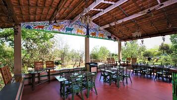 Un área de comedor al aire libre con mesas y sillas de madera, rodeada por un mural de animales.