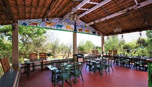 Un área de comedor al aire libre con mesas y sillas de madera, rodeada por un mural de animales.