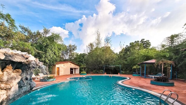 Una piscina con una formación rocosa en un lateral, un edificio pequeño y un quiosco con asientos.