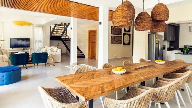 Un vaste espace de vie comprenant une table à manger en bois, des chaises en osier et un escalier menant à un niveau supérieur.