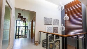 Un couloir moderne avec une rambarde en verre, des œuvres d’art accrochées au mur et un mur en bois à lattes sur la droite.
