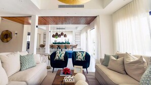 Un salon moderne avec un canapé, des fauteuils et une table basse. On aperçoit à l’arrière-plan un coin repas avec une table et des chaises.