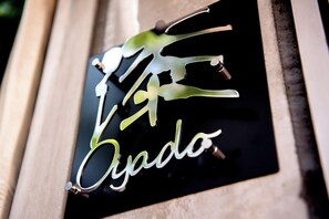 A black sign with white cursive text and a green leaf design. - Oyado Urushi (Nagasaki)