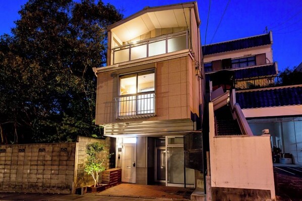 A two-story building with a balcony, a door, and a small garden area. - Oyado Urushi (Nagasaki)