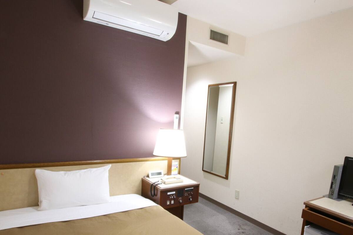 A hotel room with a bed, a desk with a computer, a phone, and a small refrigerator.
