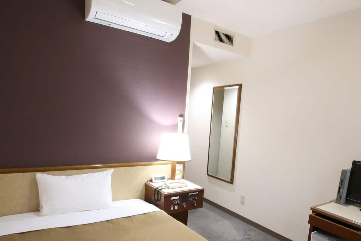 Une chambre d’hôtel équipée d’un lit, d’un bureau avec un ordinateur, d’un téléphone et d’un petit réfrigérateur.