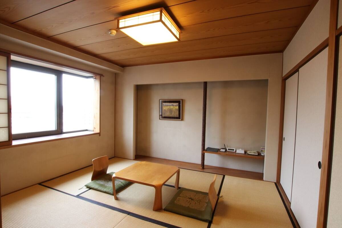 A traditional Japanese room with tatami flooring, a low wooden table, a chair, a window, and a shelf with items.
