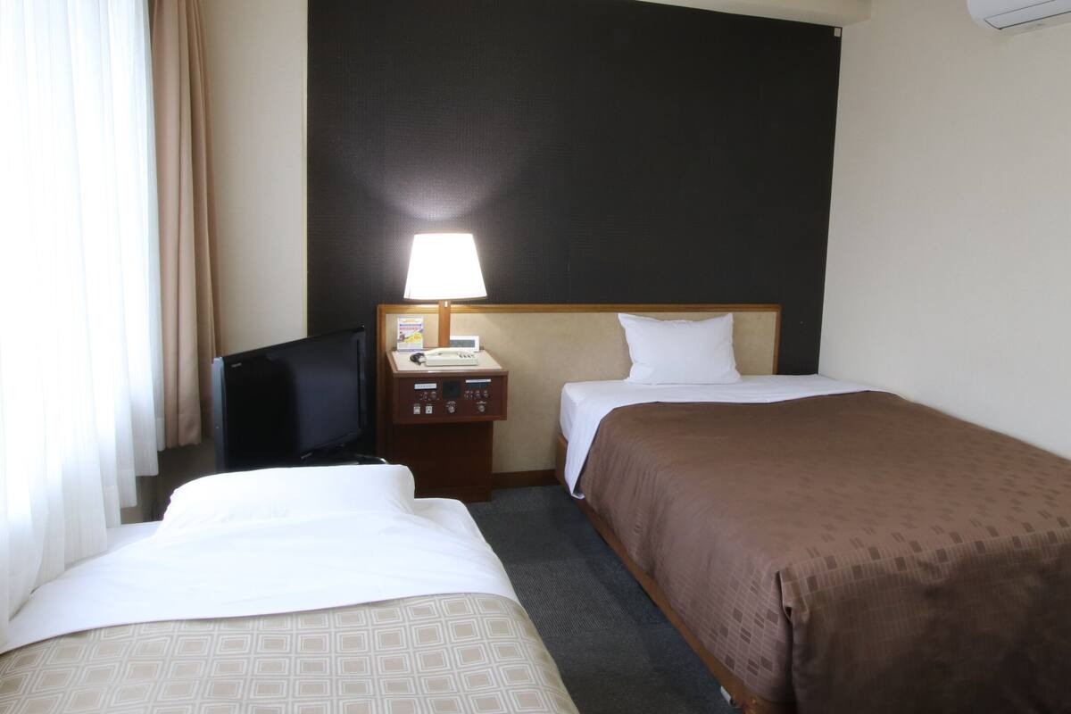 A hotel room with two beds, a desk with a lamp, a TV, and a minibar.