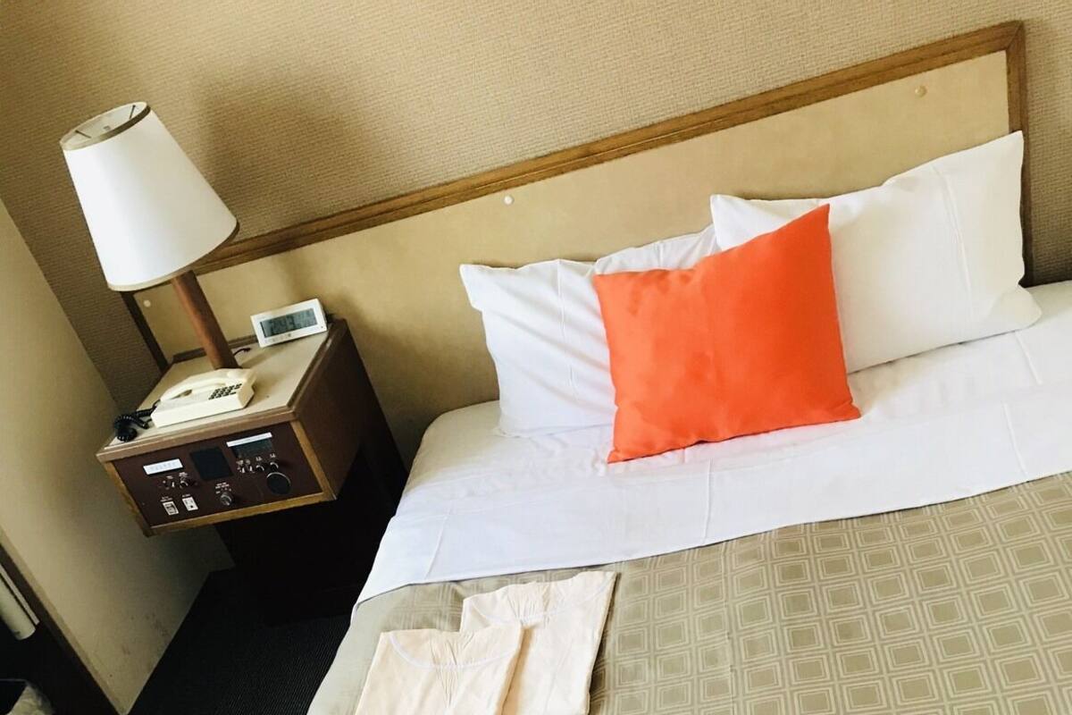 A hotel room with a bed, a nightstand with a lamp, and a telephone.