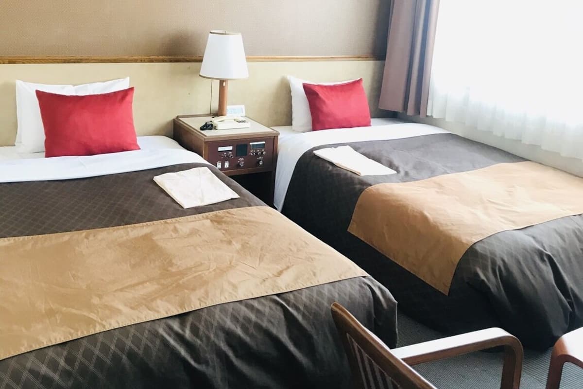Une chambre d’hôtel avec deux lits, une table de chevet avec une lampe, une chaise et une vue sur la ville par la fenêtre.