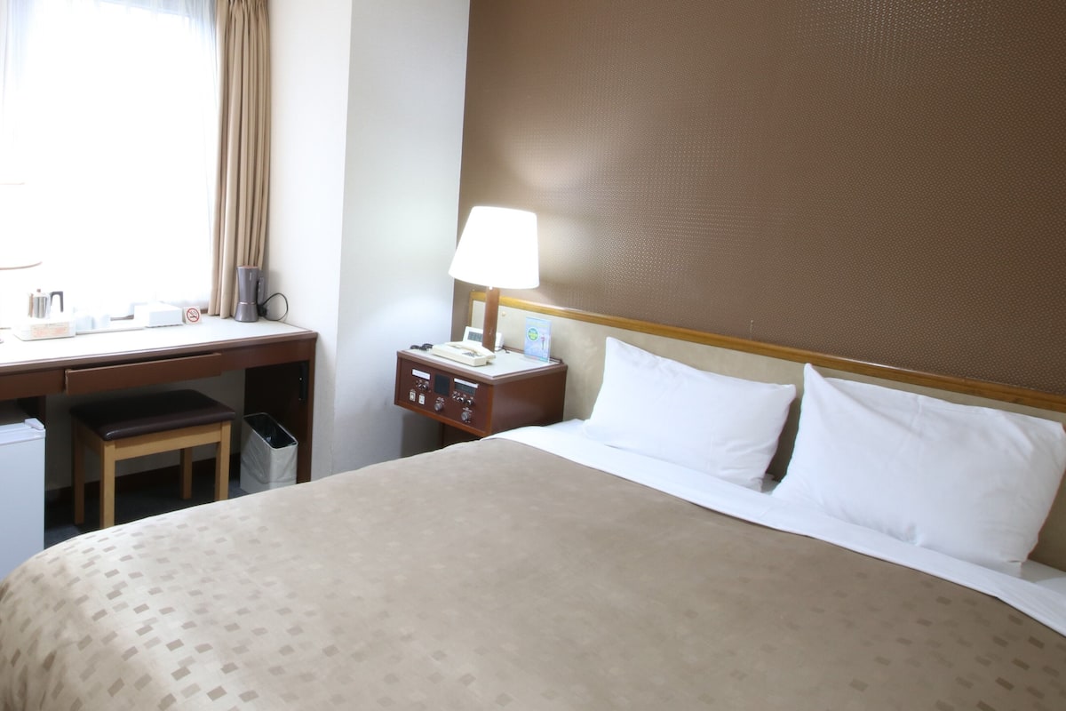 Une chambre d’hôtel comprenant un lit, un bureau, une chaise et une table de chevet avec une lampe.