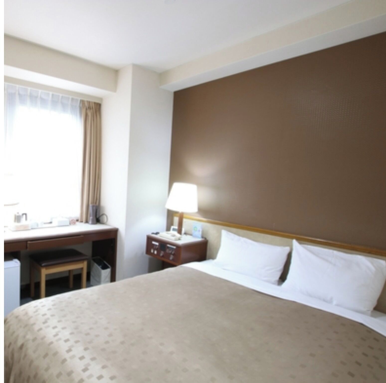 A hotel room with a bed, a desk, a chair, a nightstand, and a lamp.