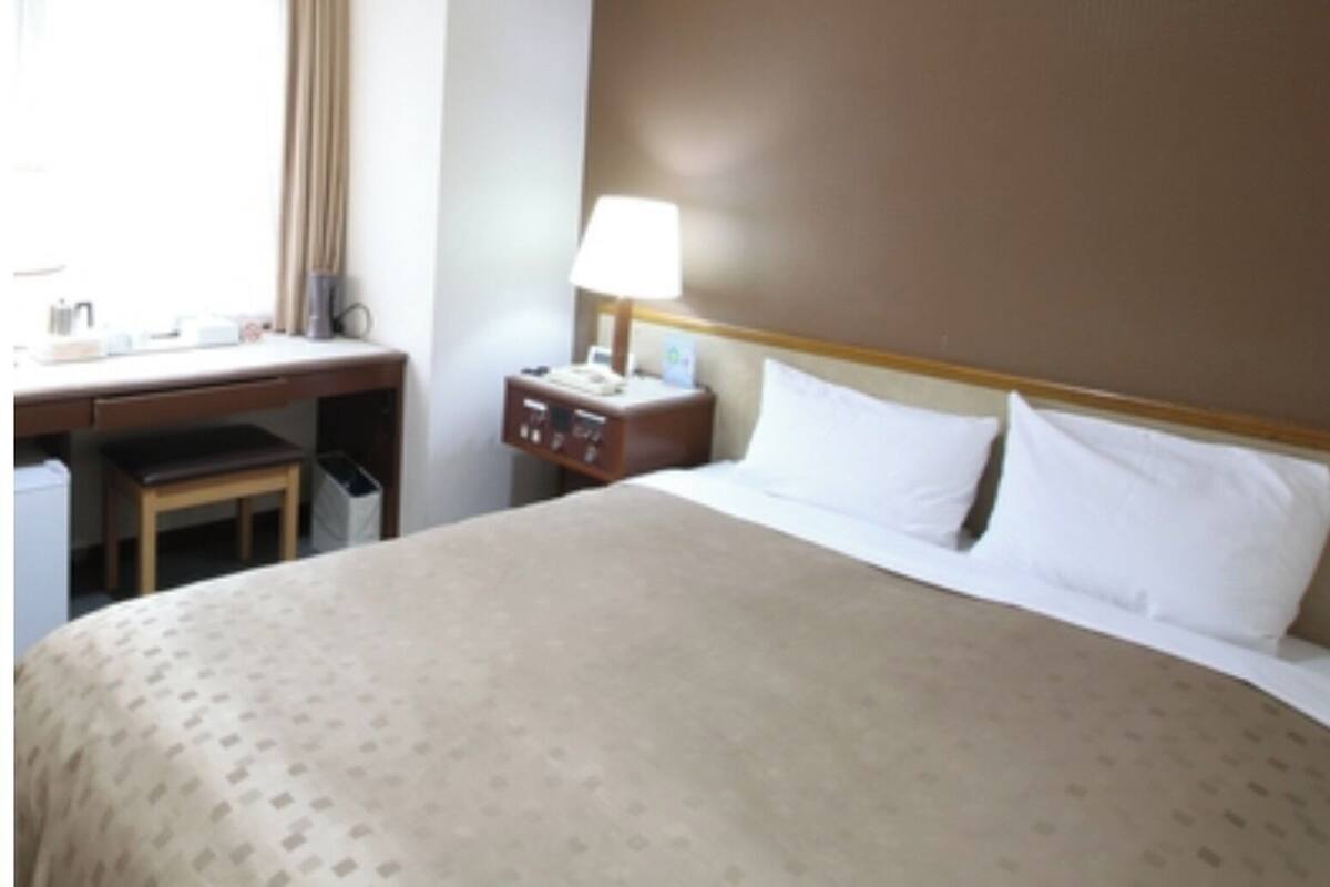A hotel room with a bed, a desk, a chair, a nightstand, and a lamp.