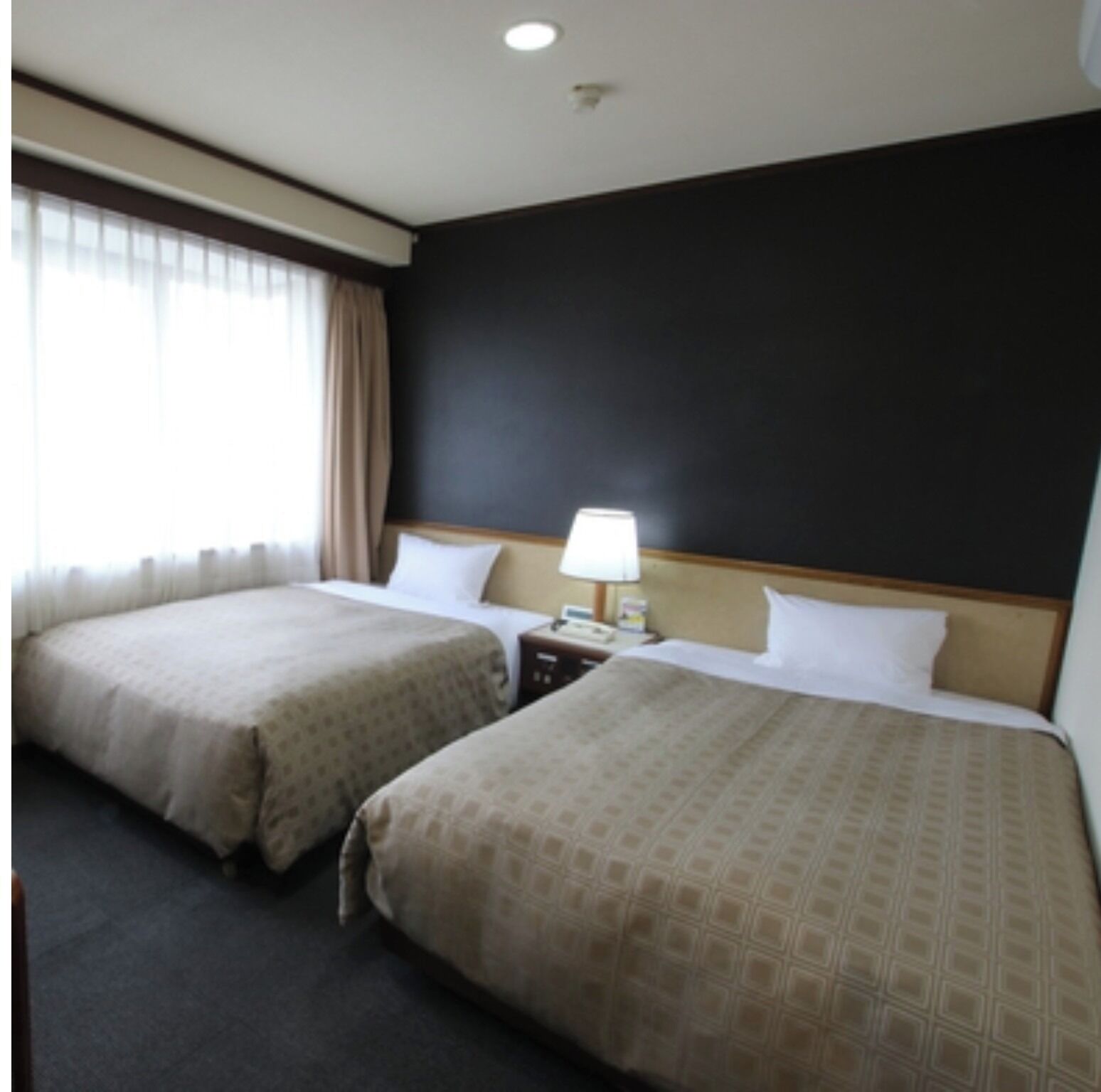 A hotel room with two beds, a nightstand, a lamp, and a window with curtains.