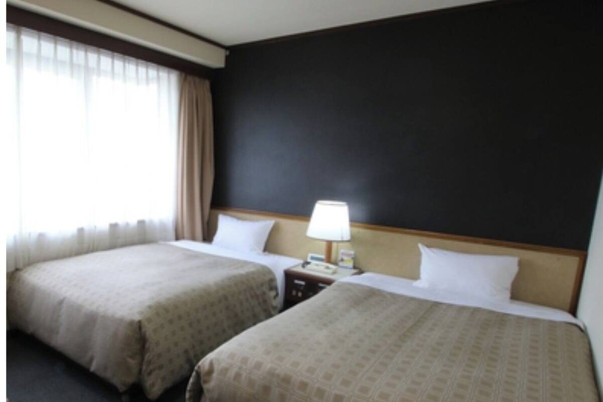A hotel room with two beds, a nightstand, a lamp, and a window with curtains.