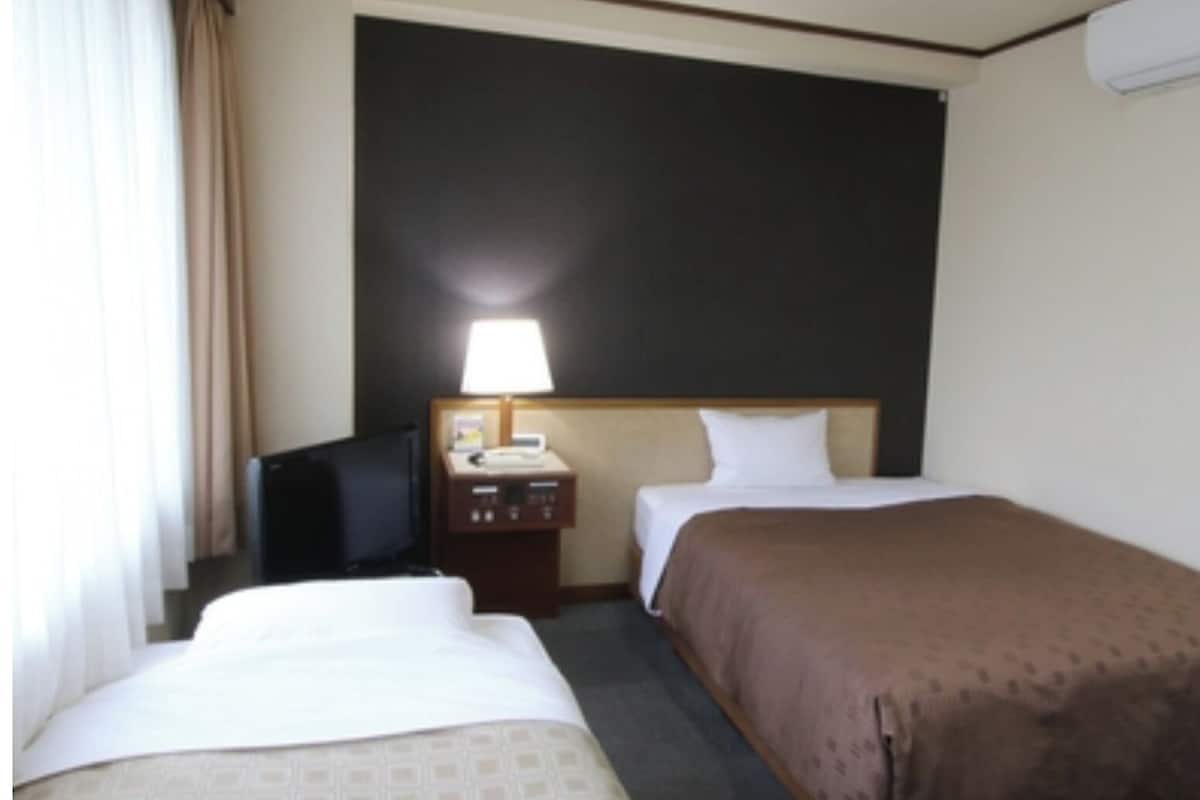 A hotel room with two beds, a desk with a lamp, a television, and a wall-mounted air conditioner.