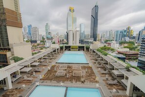 A rooftop pool area with multiple pools and lounge chairs, surrounded by high-rise buildings. - Exclusive NEW 1BR with balcony in Yoo Panama (Panamá)