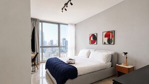Een moderne slaapkamer met een groot raam, een bed, een nachtkastje en een bureau met een stoel.
